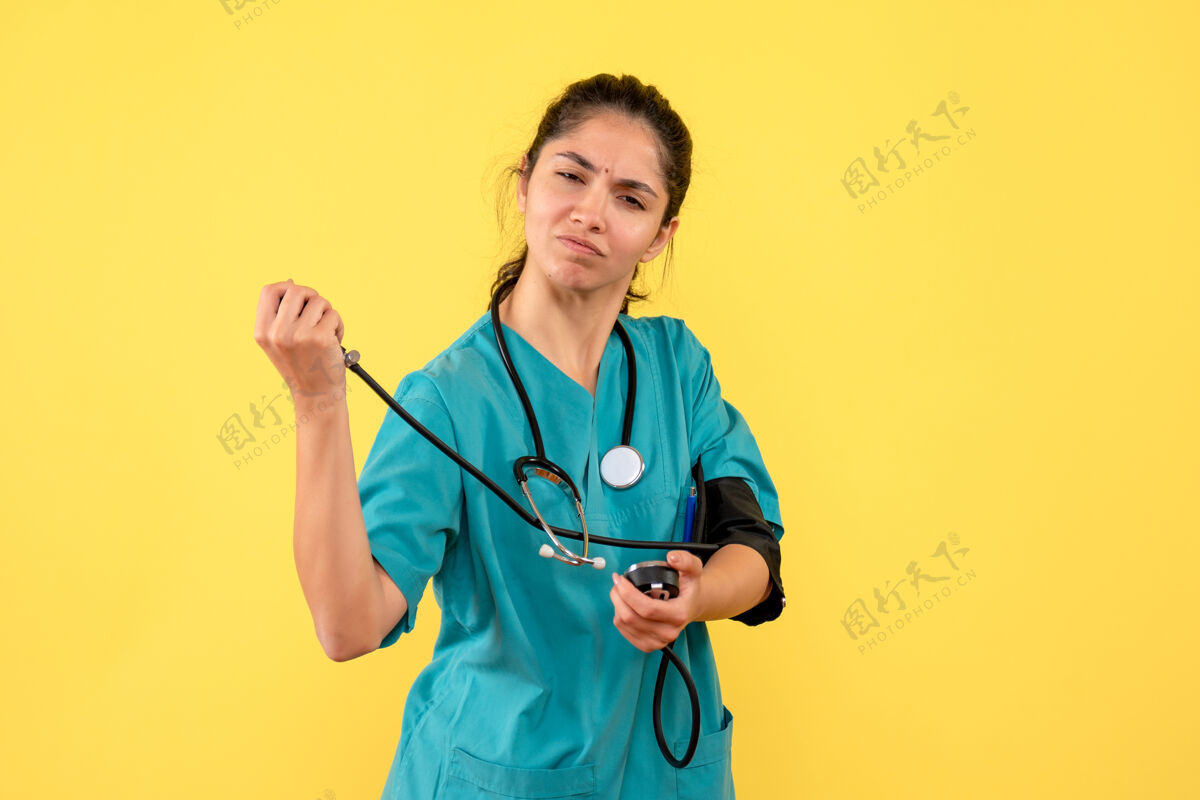 决心前视图确定女医生穿着制服使用血压计站在黄色背景上球员地点背景