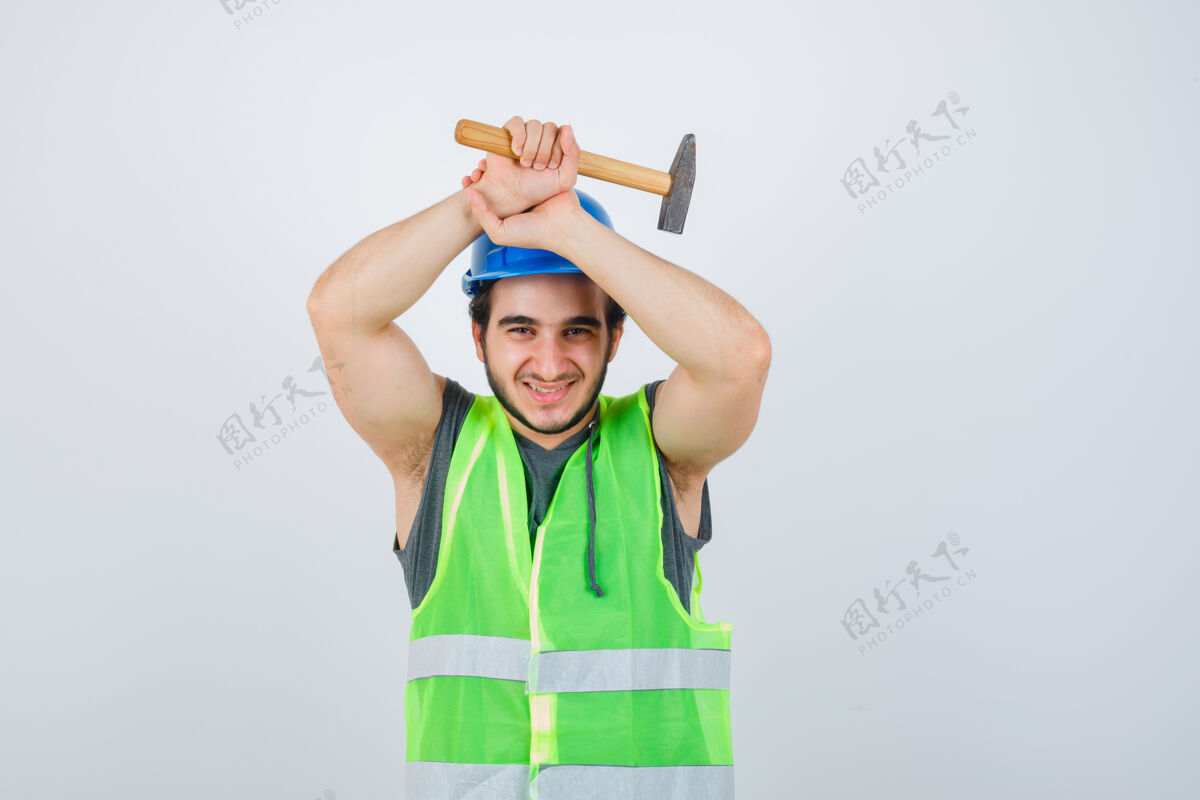 年轻年轻的建筑工人穿着工装 头上举着锤子 看上去很高兴 正对着窗外人帅气持有
