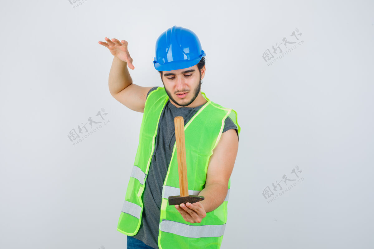 人年轻的建筑工人穿着工装手持锤子 一边举手 一边仔细看 正前方表情持有提高