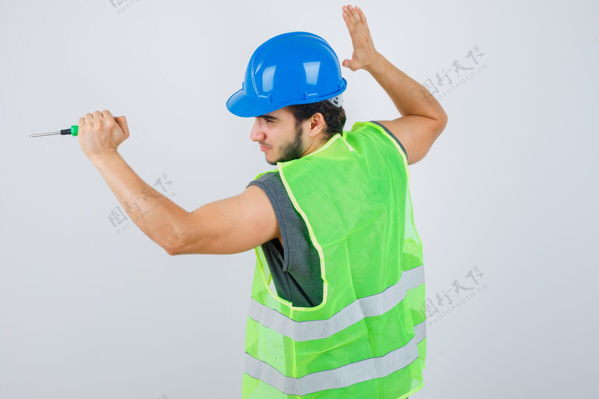 不高兴身穿制服的年轻建筑工人举起手来用螺丝刀敲打 看上去很疯狂 正前方视图人人压力