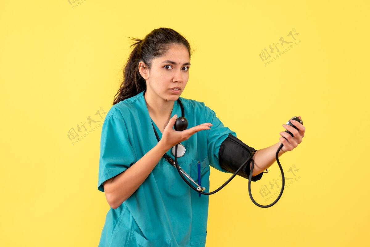 手持正面图黄色背景上穿着制服手持血压计的美丽女医生医学成人肖像