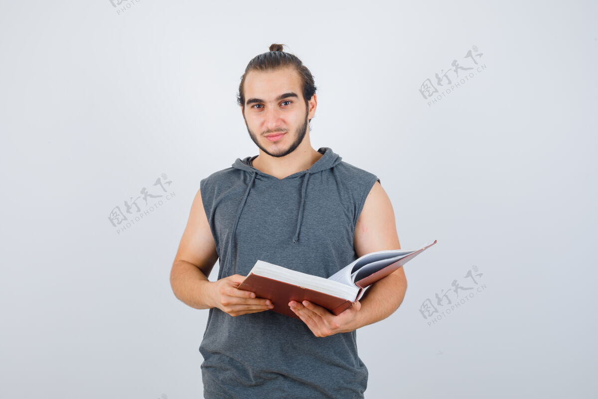 前年轻的男性拿着书 穿着无袖连帽衫看着相机 看起来很帅前视图健康强壮思想