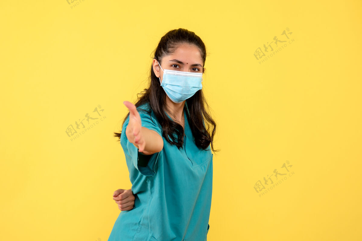 微笑正面图身着制服的年轻女医生一只手放在背后站在黄色背景上人物面具背面