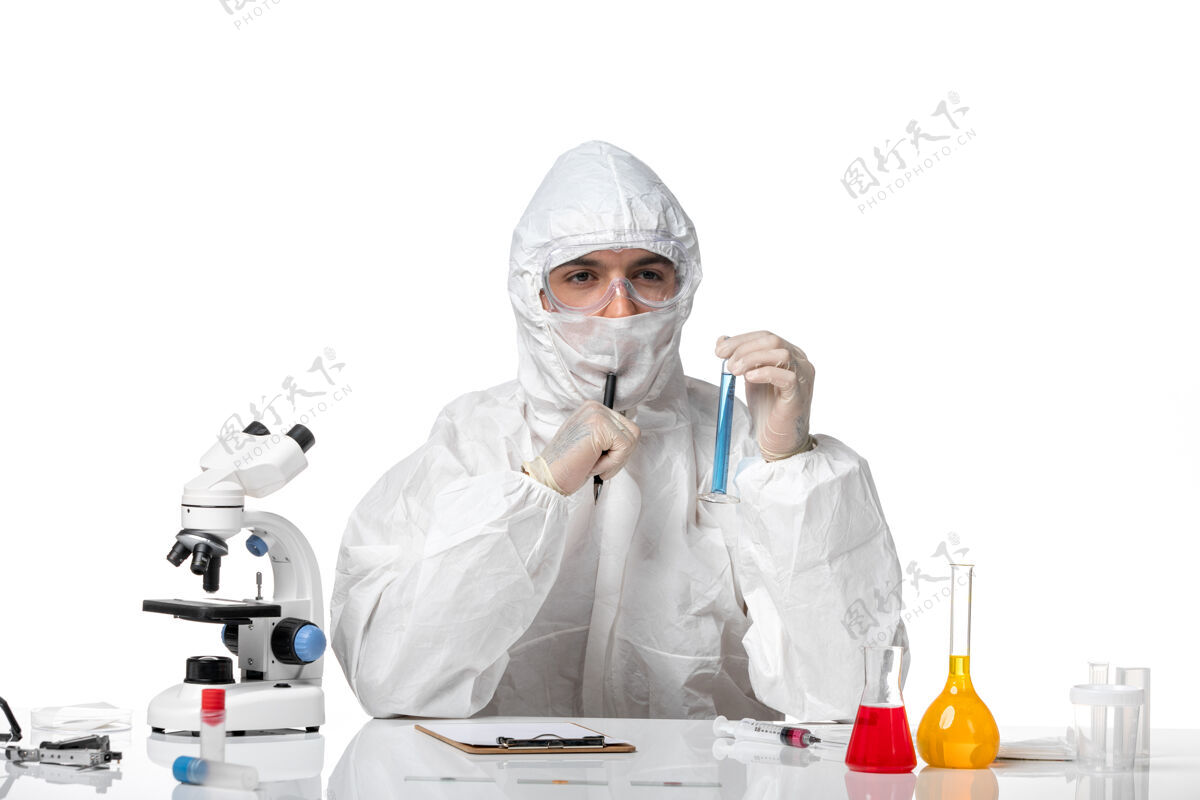 医生正面图：男医生穿着防护服 戴着口罩 在浅白的桌子上拿着装有蓝色溶液的瓶子口罩前保温瓶