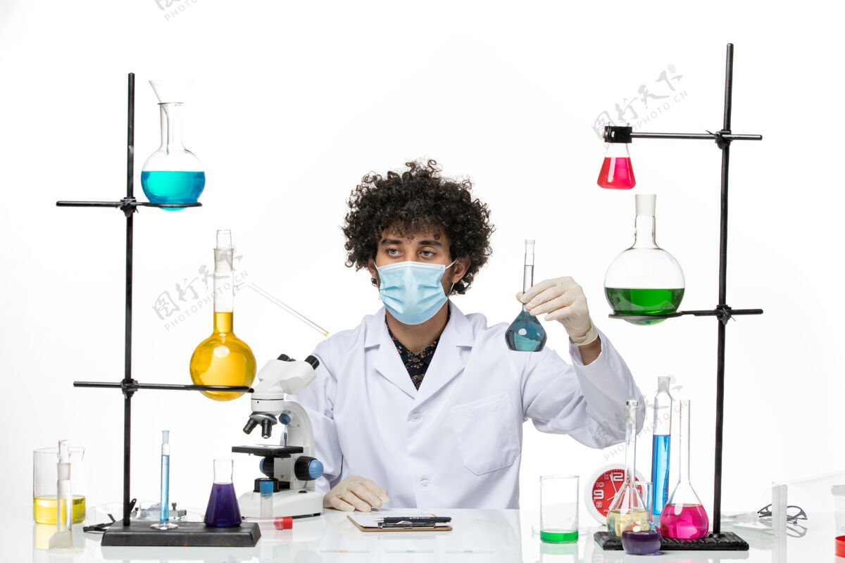 医学正面图：男药剂师穿着白色的医疗服 戴着面罩 白色的桌子上放着蓝色的溶液正面男性医学