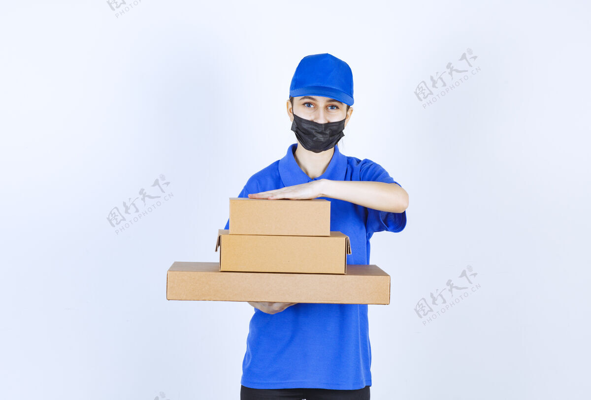 送货戴着面具和蓝色制服的女信使手里拿着一堆纸箱安全促销姿势