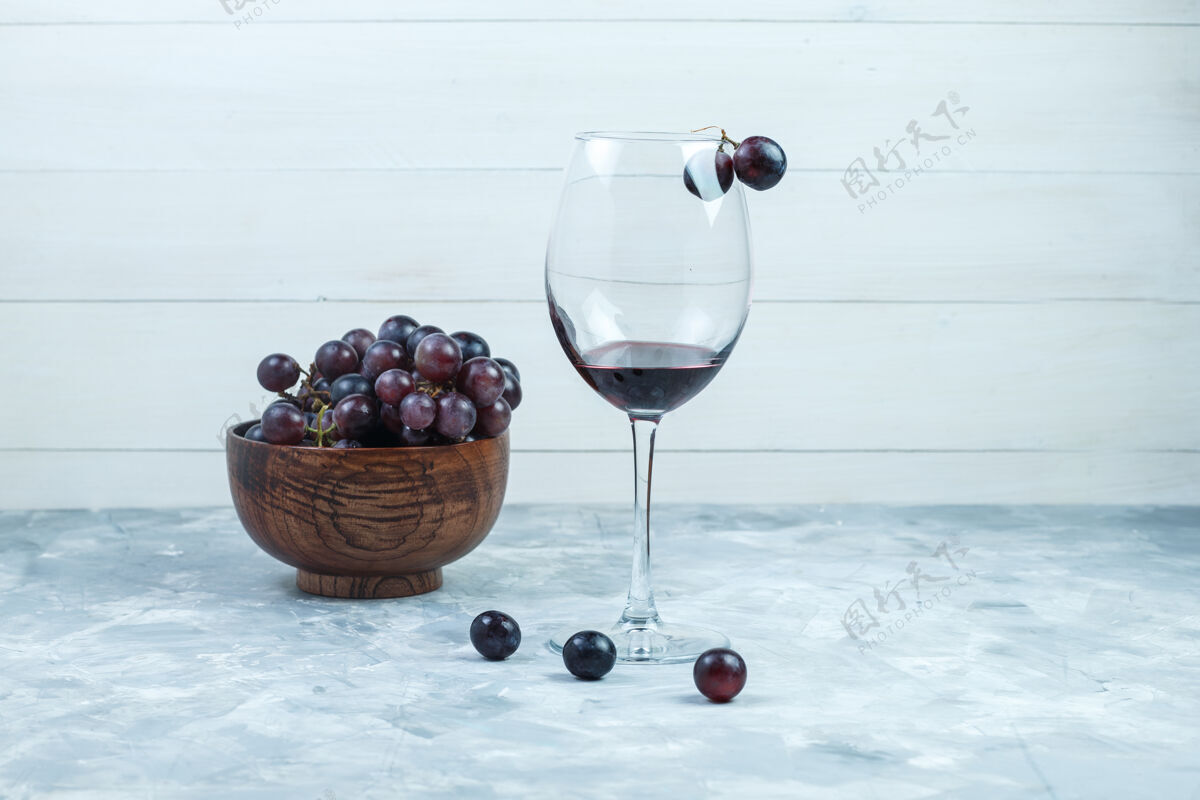 自然一杯葡萄酒和黑葡萄放在一个粘土碗里 背景是灰色和木质的侧视图葡萄藤健康有机