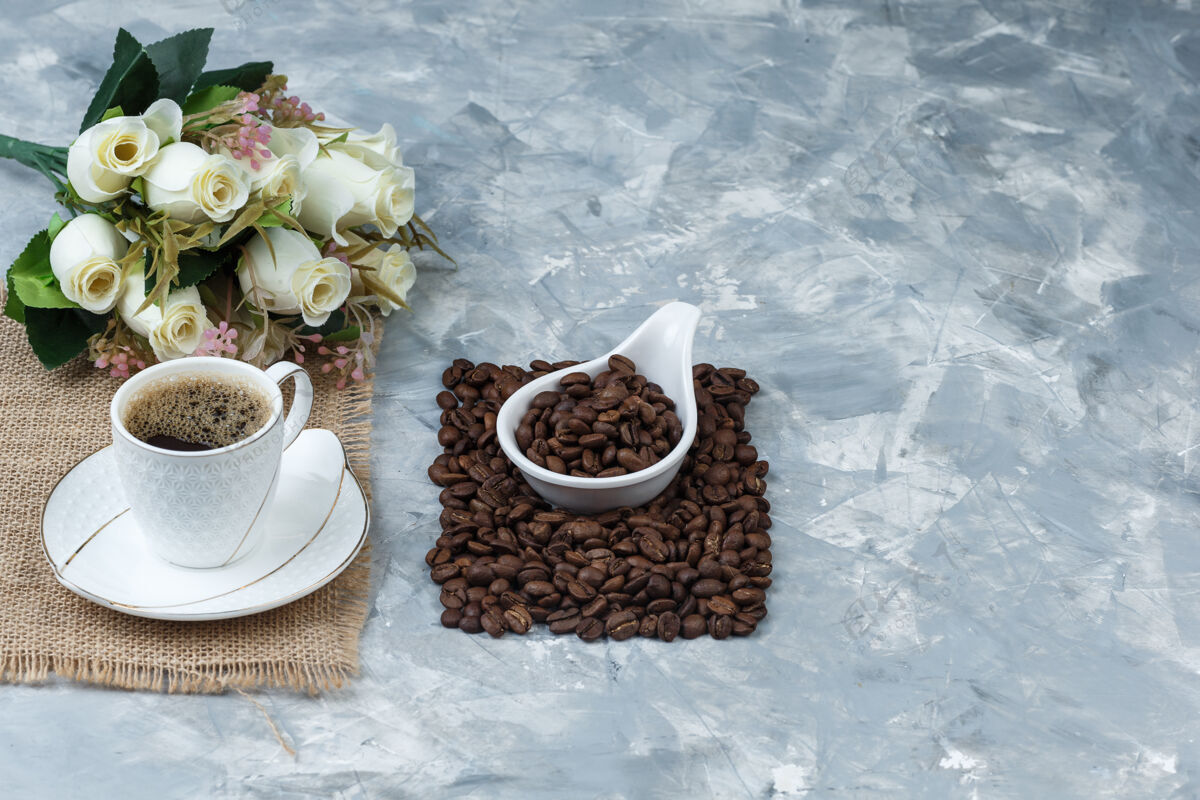 餐桌咖啡豆放在一个白色的瓷壶里 里面放着一杯咖啡 一个布袋 蓝色大理石背景上的花朵高角度观看热浓缩咖啡件