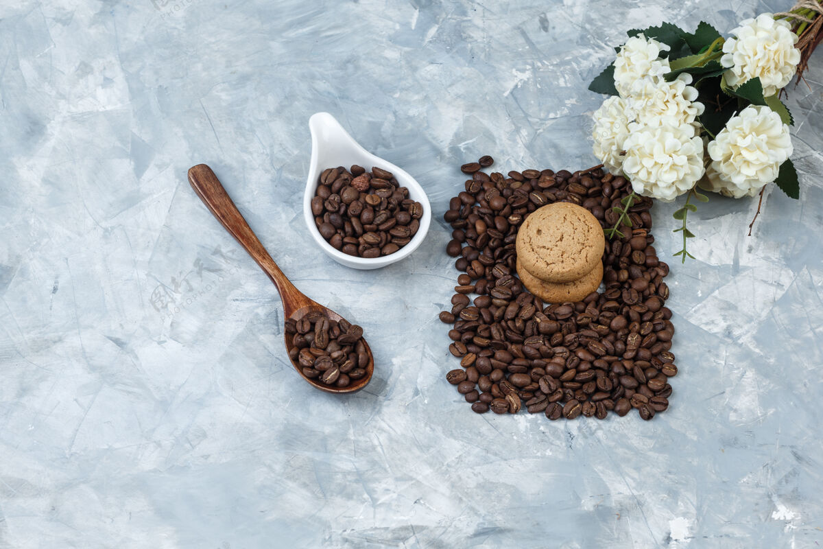 想法把咖啡豆放在木勺里 白色瓷壶里放着饼干 浅蓝色大理石背景上放着花水平人花大理石