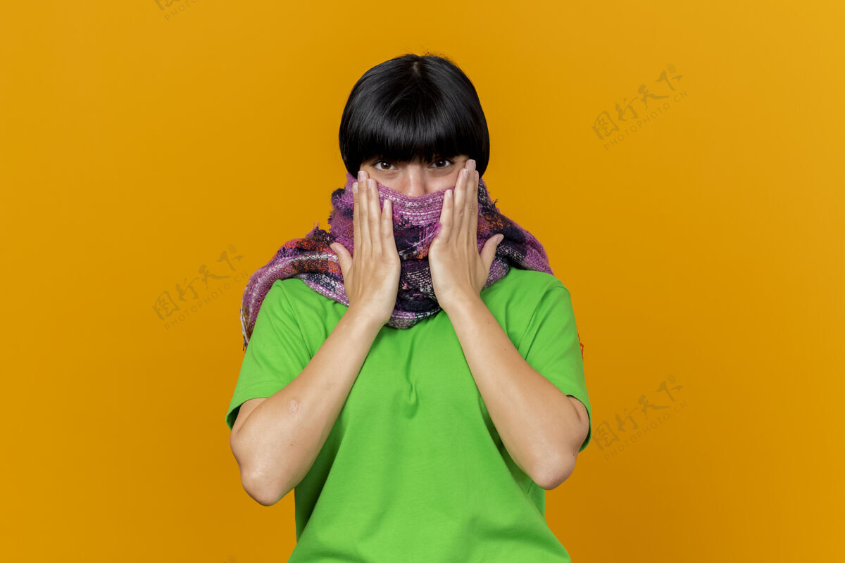 年轻年轻生病的白人女孩戴着围巾 用围巾遮住嘴 手放在围巾上 隔离在橙色的墙上 留着复制空间盖穿围巾