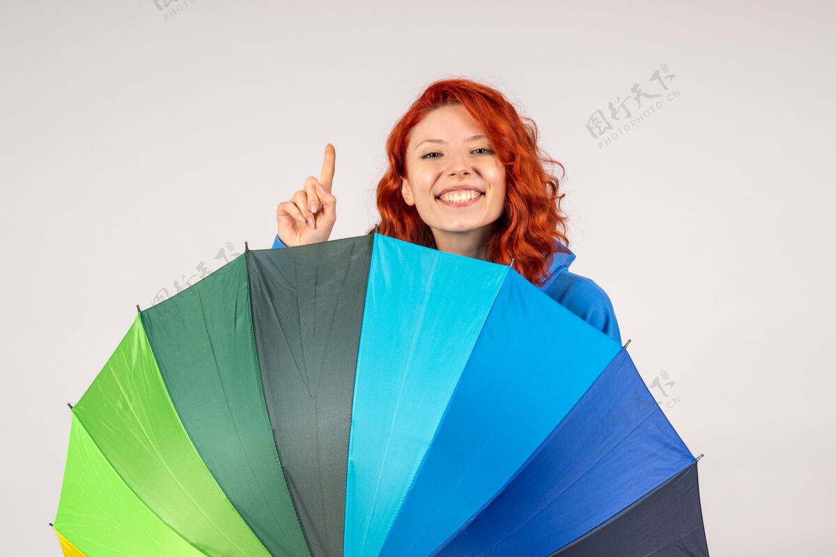 女人白色墙壁上带着彩色雨伞的年轻女性的正视图多彩彩虹快乐