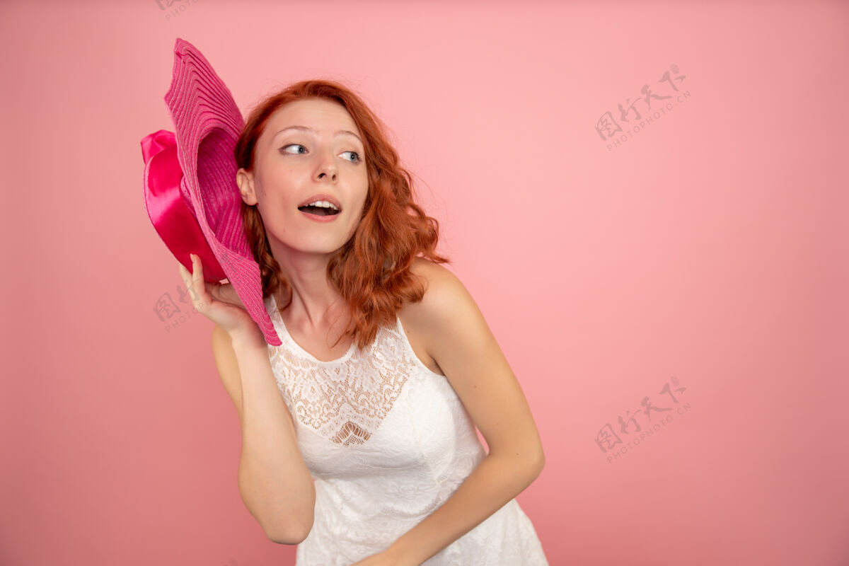 年轻女性前视图的年轻女性与粉红色的墙壁上的粉红色帽子摆姿势模型人可爱