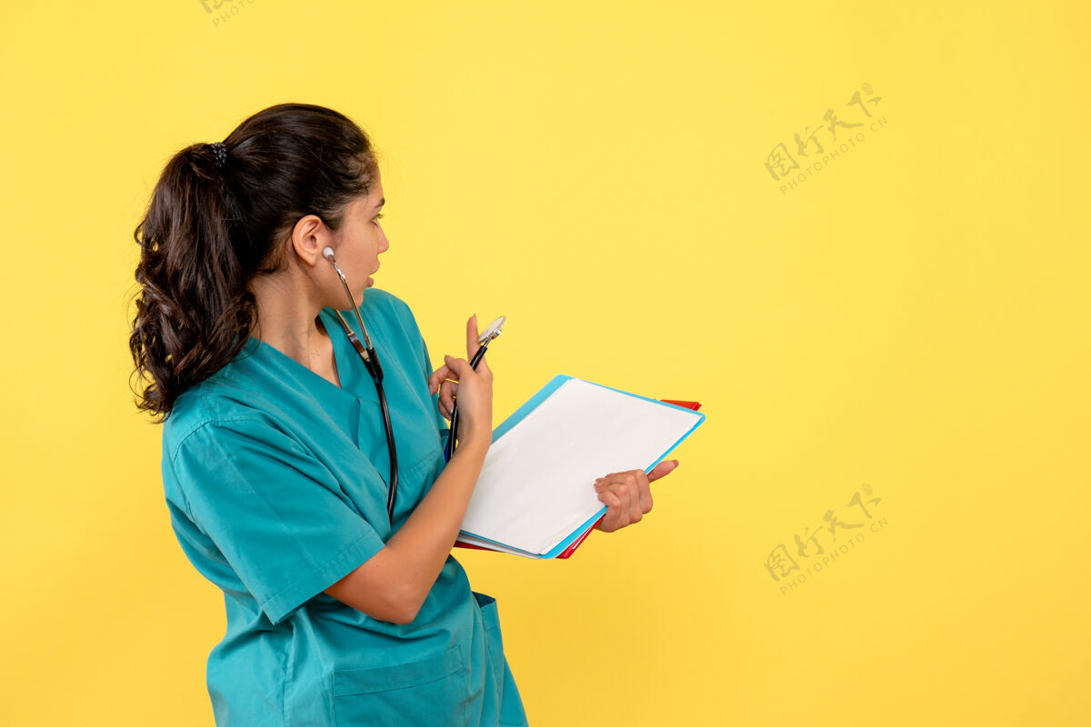 快乐穿着制服的女医生正拿着黄墙上的纸看着后面肖像微笑封面