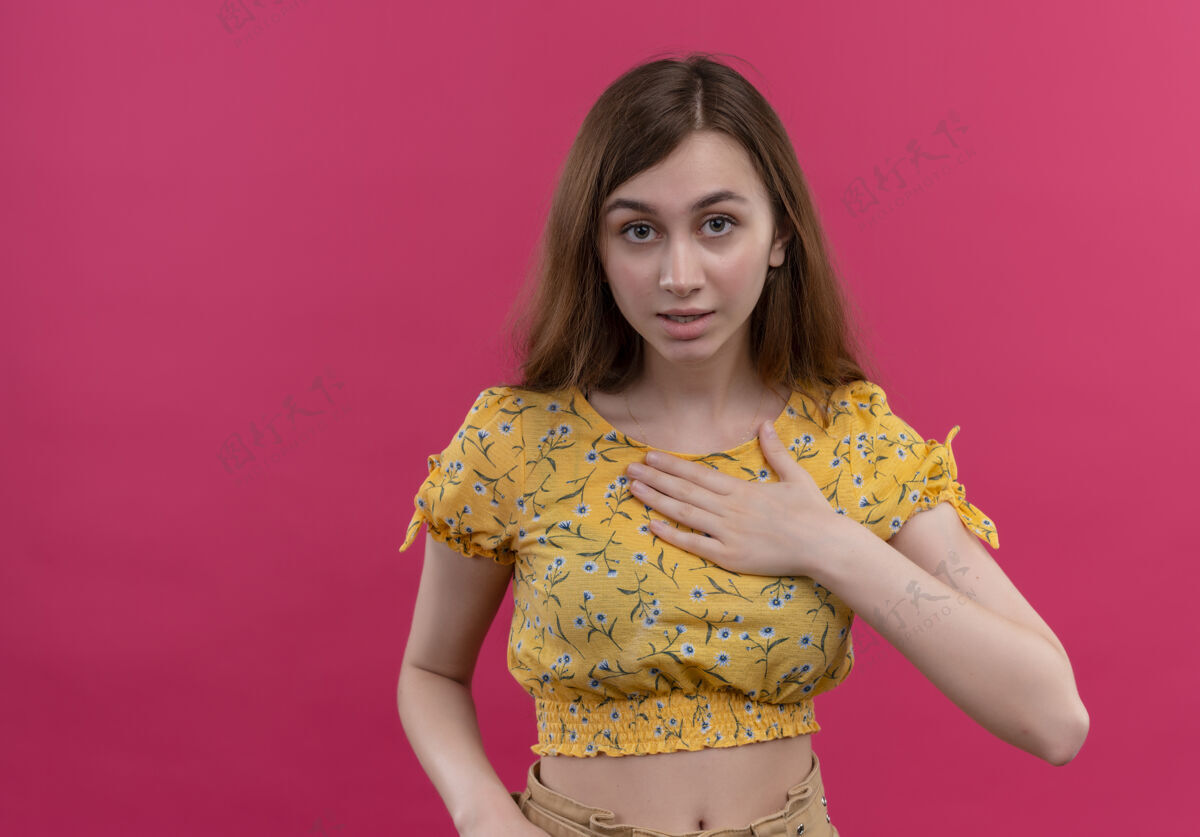 手惊讶的年轻女孩把手放在孤立的粉红色墙壁上的胸部与复制空间胸部年轻女孩