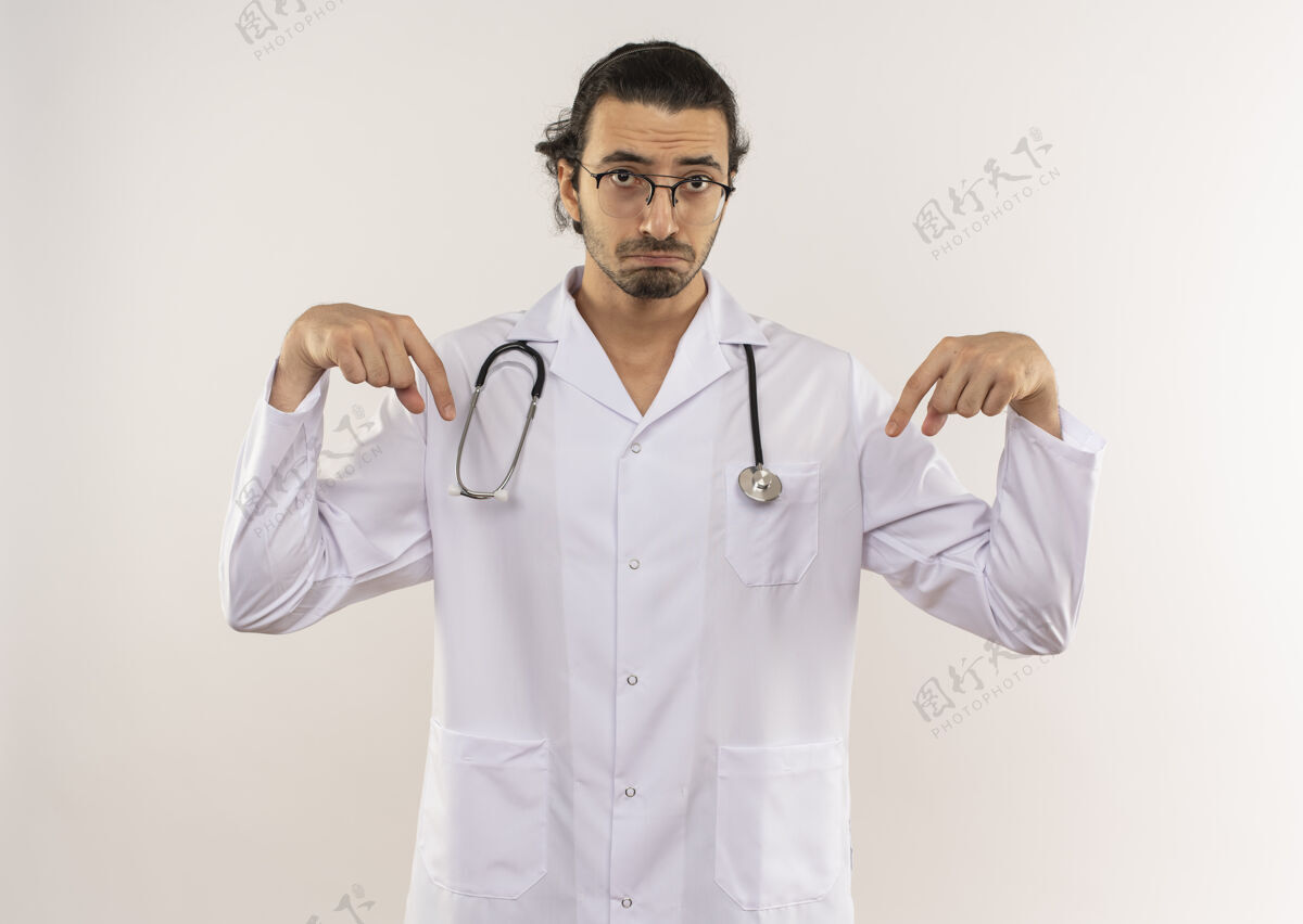 年轻悲伤的年轻男医生戴着眼镜 穿着白色长袍 用听诊器指着下面隔离的白墙上有复印空间听诊器眼镜光学