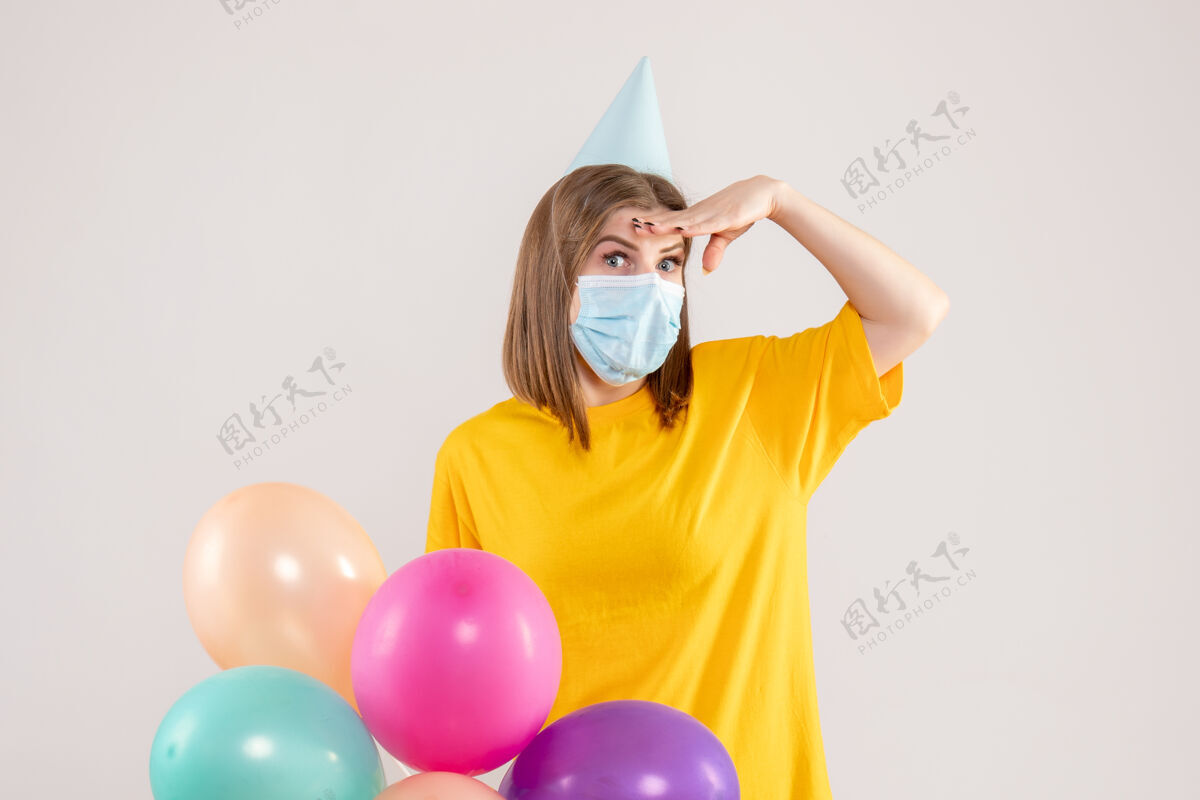 健康戴着白色面具手持彩色气球的年轻女性庆祝生日举行