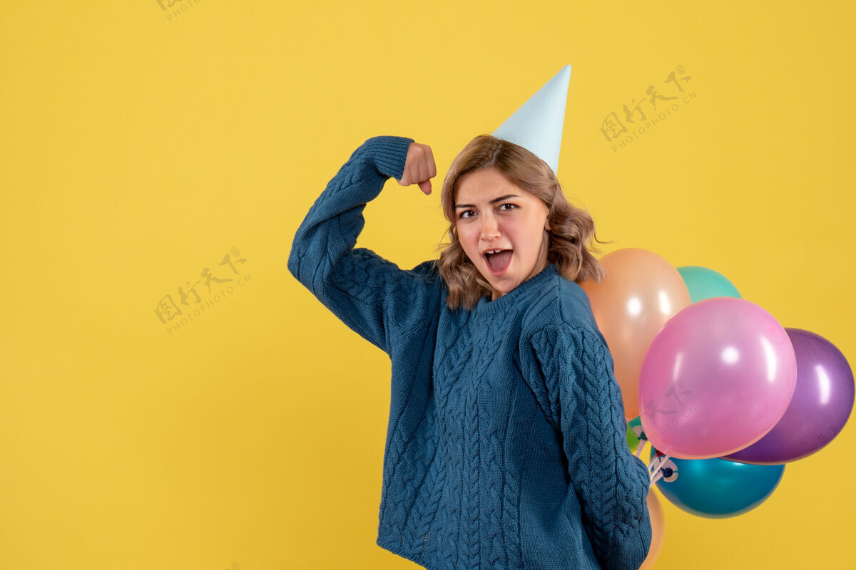 生日年轻的女性把五颜六色的气球藏在黄色的背上人们背面视图