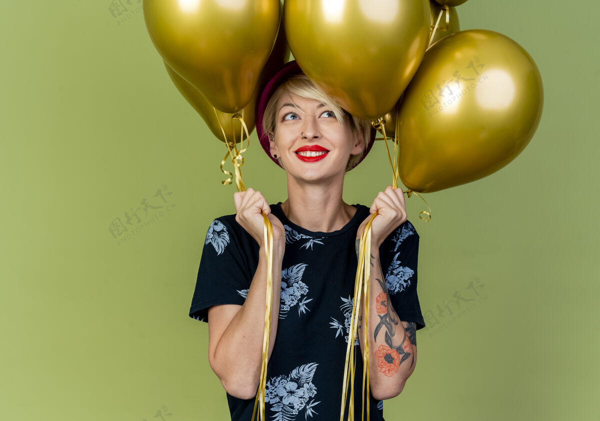 气球微笑着的年轻金发派对女孩拿着气球看着一边孤立的橄榄绿背景与复制空间抱着侧线年轻