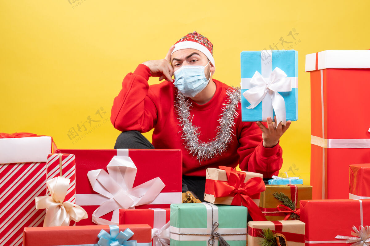 人正面图：年轻男性围坐在黄色背景上的圣诞礼物旁礼物坐着微笑