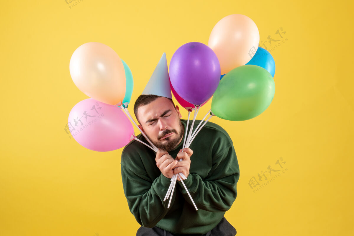 年正面图黄色背景上手持彩色气球的年轻男性气球公园地区