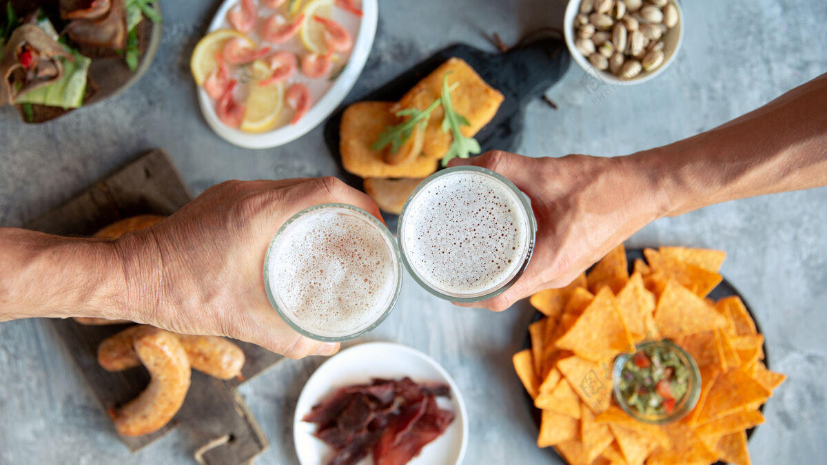泡沫两只手拿着啤酒杯和美味小吃的俯视图桌子酒精庆典
