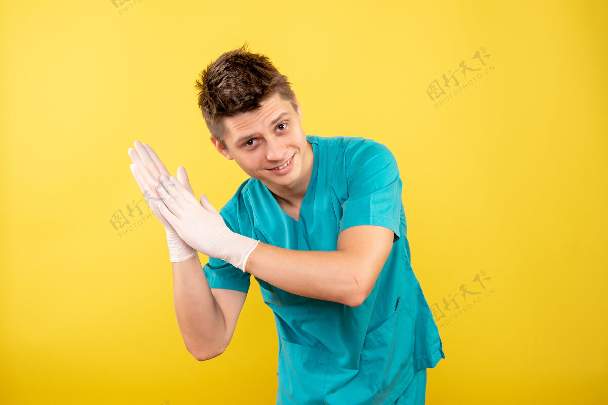 微笑正面图年轻的男医生穿着医疗服 戴着手套在黄色背景上鼓掌年轻男医生手套医疗