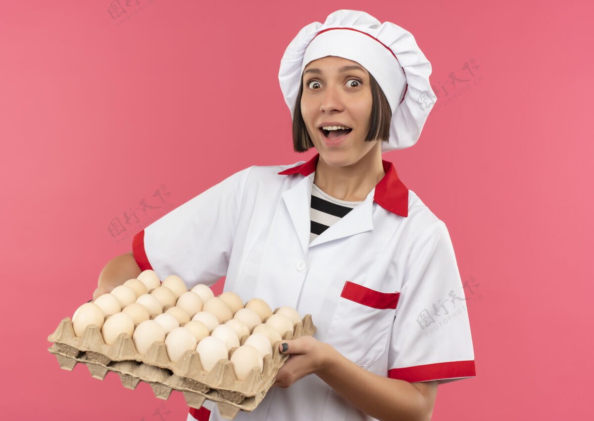 女年轻的女厨师穿着厨师制服 手里拿着一盒粉红色的鸡蛋纸箱持有制服