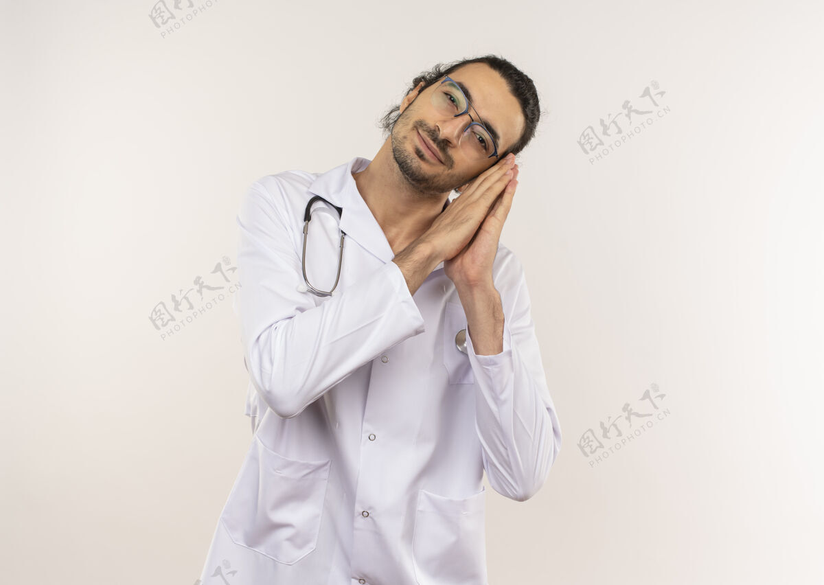 手势年轻的男医生戴着眼镜 穿着白色长袍 听诊器 在隔离的白色墙壁上显示睡眠姿势 并留有复印空间男性请穿