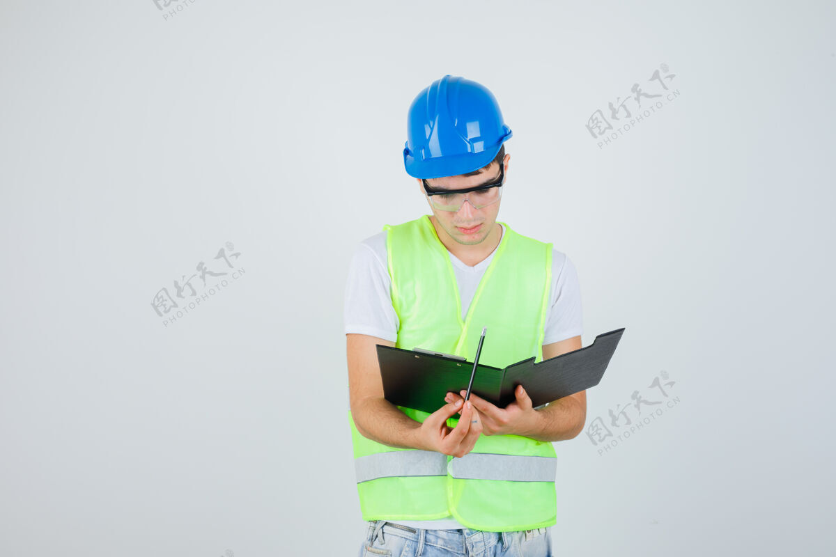 笔记年轻的男孩穿着建筑制服在剪贴板上读笔记 看上去很专注 正对着前方看父母儿子乐趣