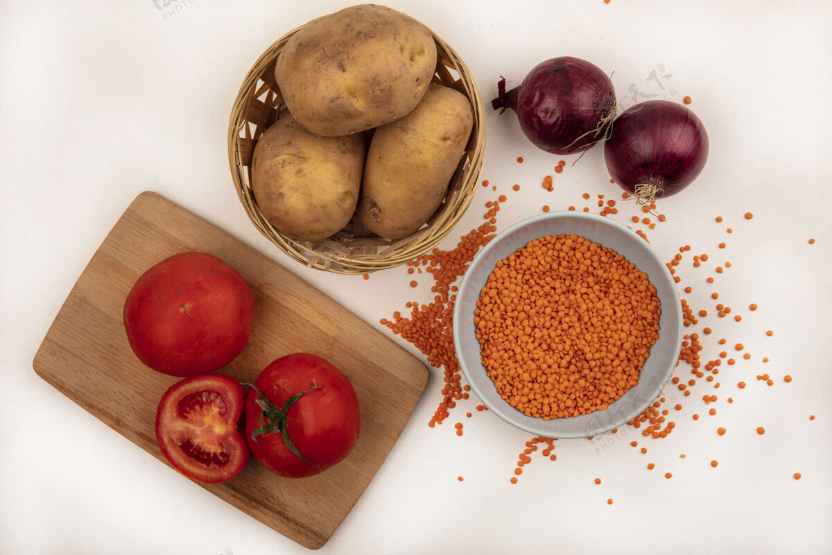 桶顶视图：明亮的橙色小扁豆放在碗里 土豆放在桶里 西红柿放在木制的菜板上 红洋葱被隔离在白色的墙上颜色明亮土豆