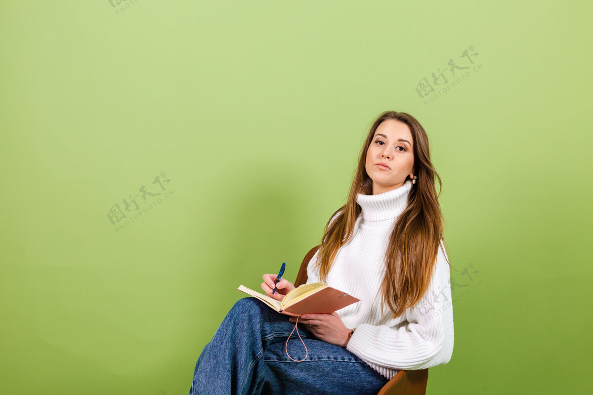 情感漂亮的欧洲女人穿着休闲的白色毛衣孤立 可爱快乐的坐在椅子上用记事本和笔狡猾思想学习