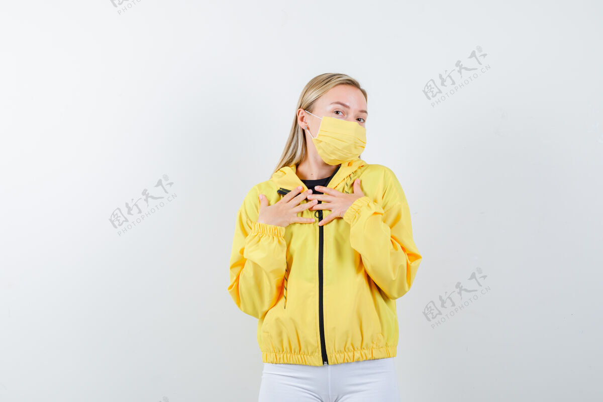 健康年轻的女士穿着夹克 裤子 戴着面具 双手放在胸前 看起来很感激 前视图自然金发漂亮