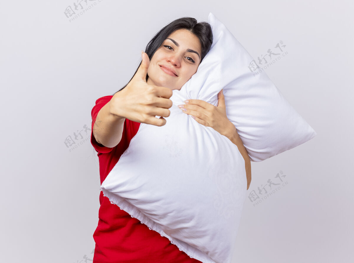 疾病高兴的年轻白种人生病的女孩抱着枕头看着相机显示拇指向上孤立的白色背景与复制空间复制请枕头