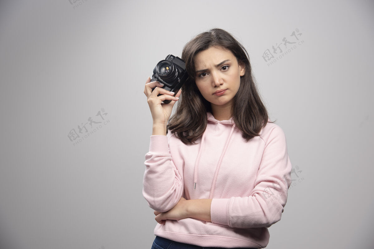 摄影师穿着粉色运动衫的年轻女子拿着相机生气地看着人可爱肖像