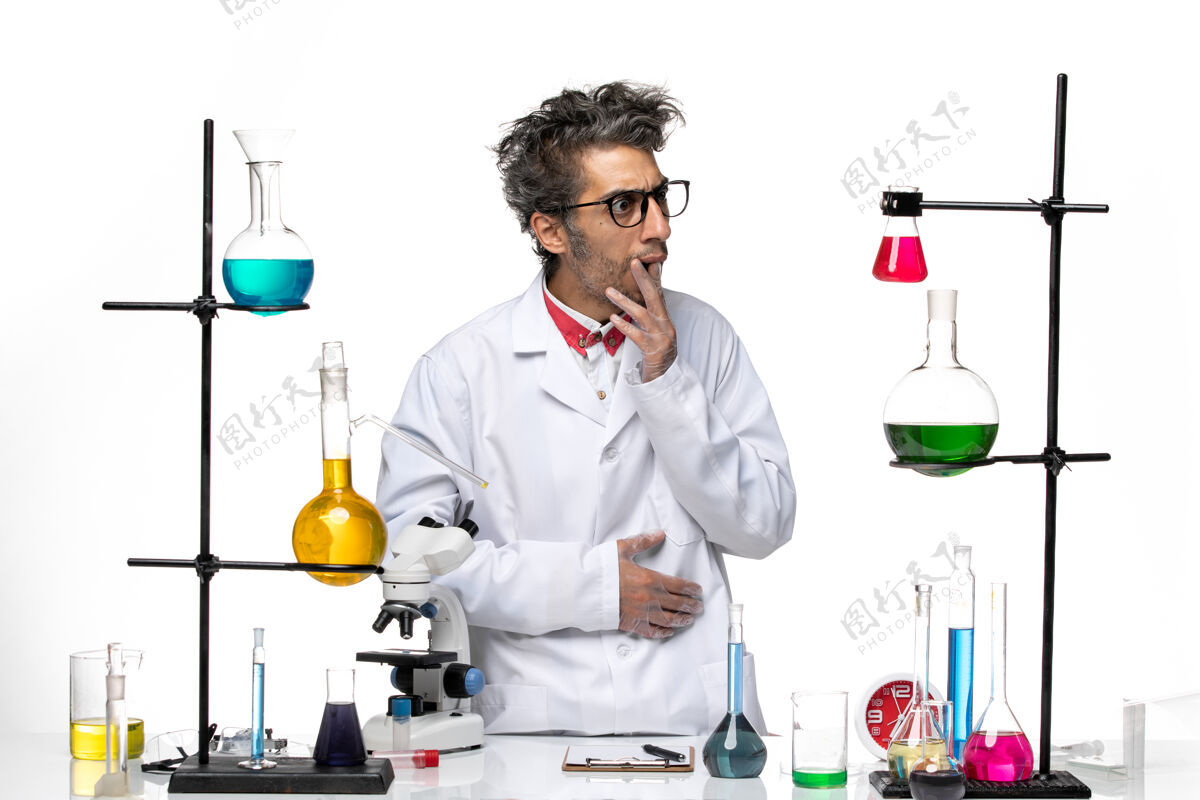 专业正面图穿着白色医疗服的男科学家站在桌子前拿着解决方案立场实验室化学