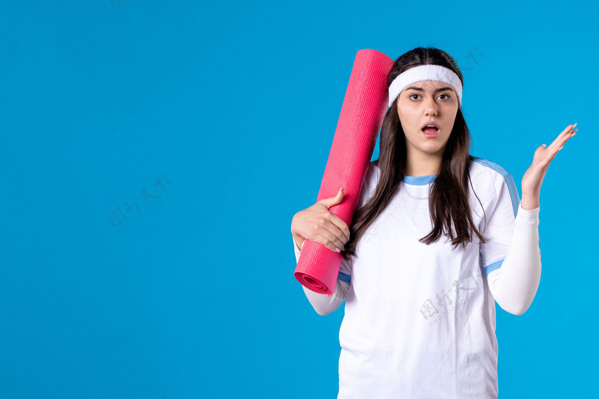 微笑前视图：年轻女性 带着地毯在蓝色墙壁上练习人物健身房成人