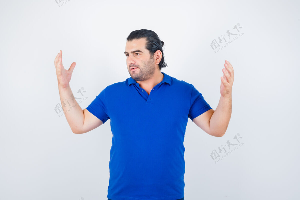专业身着蓝色t恤的中年男子举手的肖像 正看着若有所思的前视图随意年龄坐着