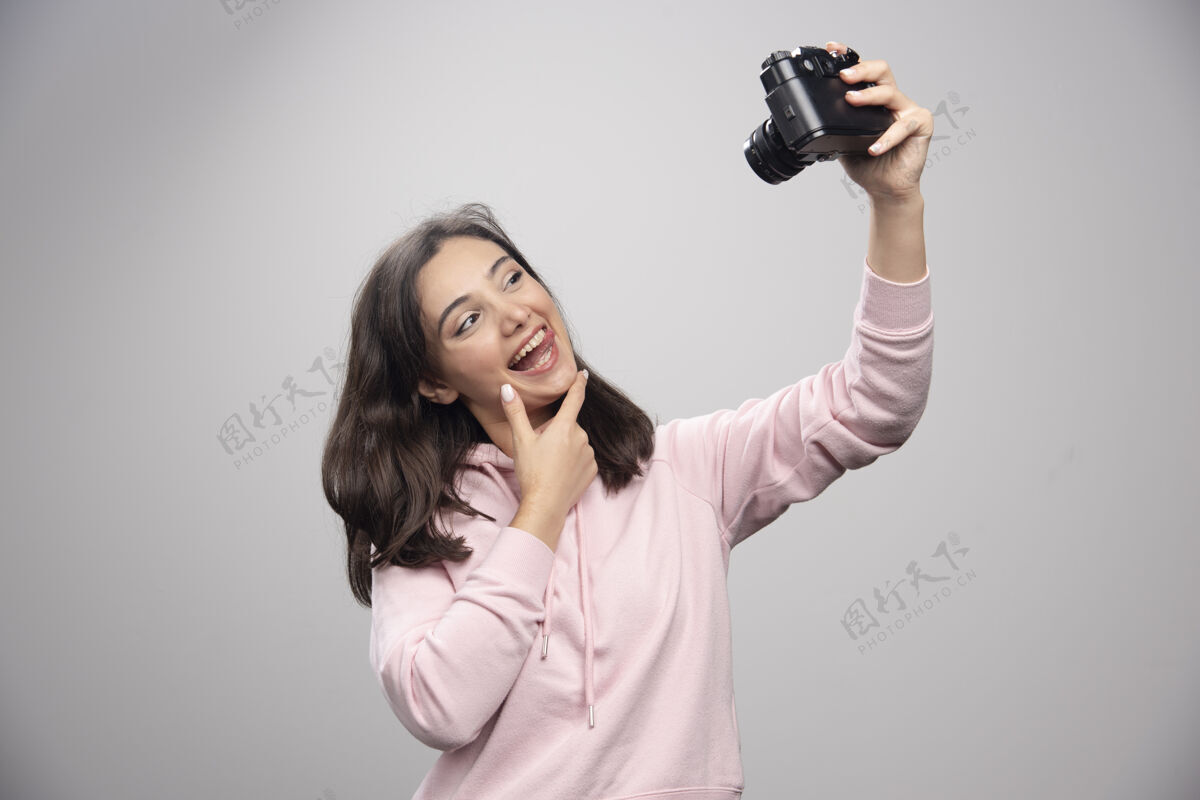 人漂亮的年轻女子在灰色的墙上用相机自拍漂亮女人女人