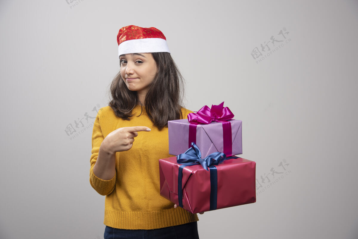 庆祝带着圣诞礼物的戴圣诞帽的年轻女子欢呼乐趣表情