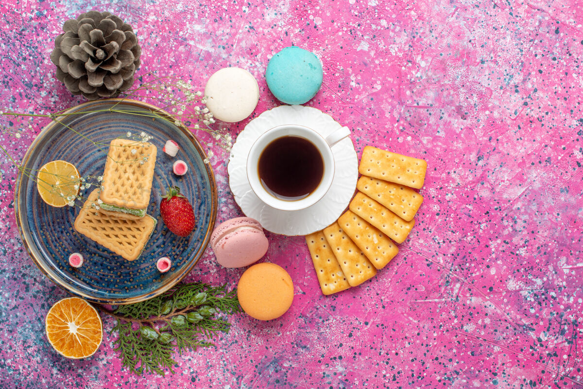 食物美味的华夫饼和法式麦卡龙饼干的俯视图 粉红色的表面上放着茶麦卡龙饼干咖啡