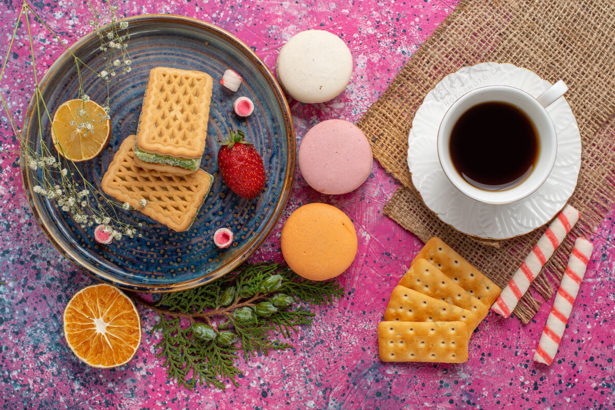 化妆品浅粉色表面上有麦卡龙茶和棉花糖的美味华夫饼俯视图糖饼干顶视图