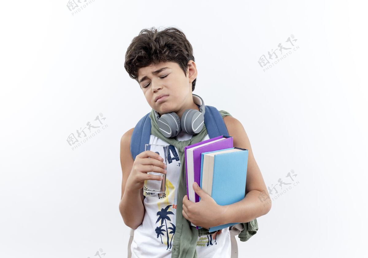 耳机闭上眼睛悲伤的小男生背着书包 戴着耳机 手里拿着一杯水和一本书 孤零零地放在白色的纸上包举行白