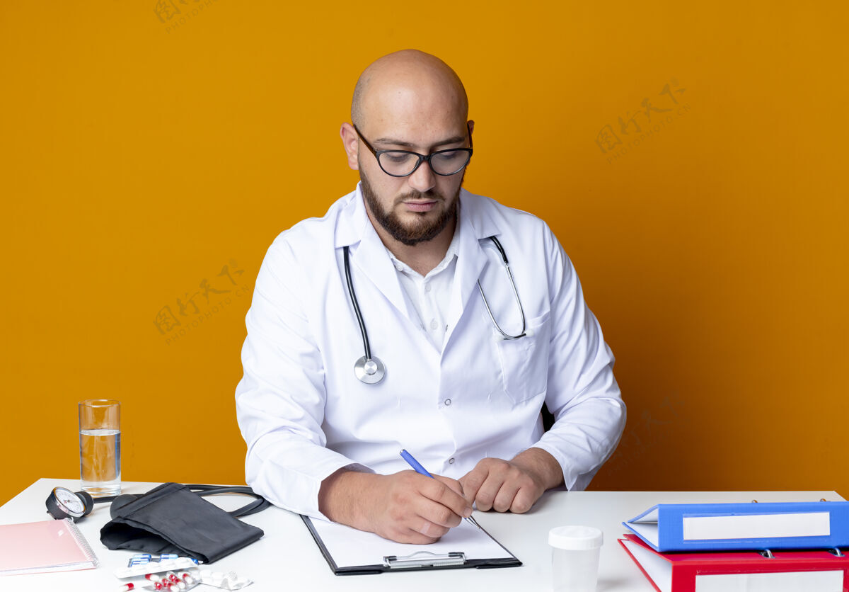 秃头年轻的秃头男医生穿着医用长袍戴着听诊器坐在工作台上医疗橙色男性
