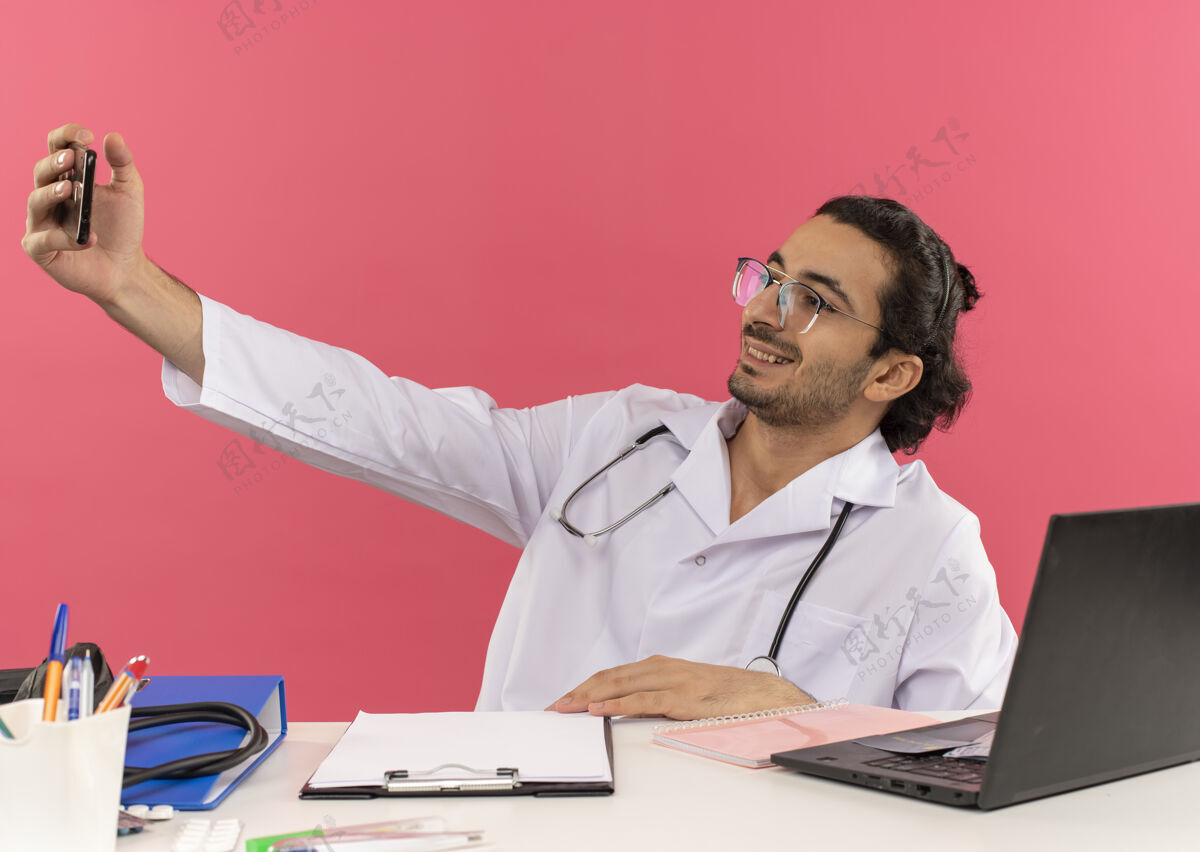 自拍微笑的年轻男医生戴着医用眼镜 穿着带听诊器的医用长袍桌子男人男性