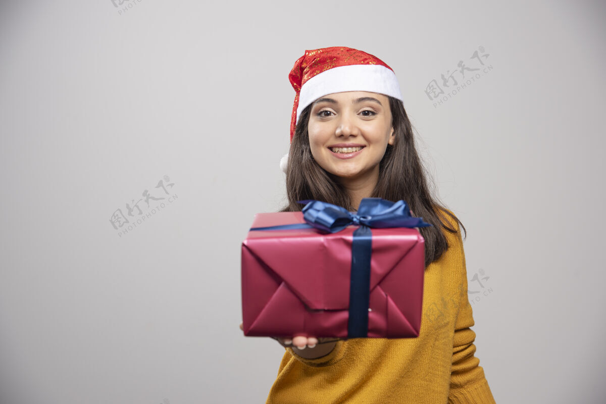 礼品盒戴着圣诞帽的微笑女人展示着一个礼品盒帽子女性微笑