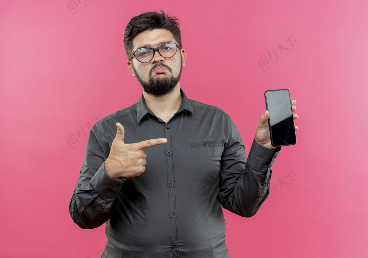 商人悲伤的年轻商人戴着眼镜拿着手机指着粉色的隔离带年轻握表情