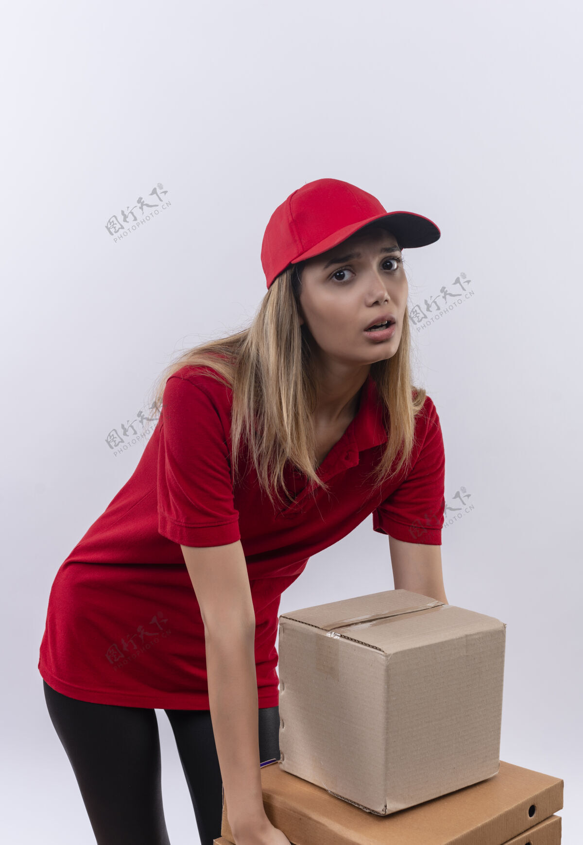交货紧张的年轻送货女孩穿着红色制服 戴着帽子 试图拿着许多箱子隔离在白色年轻制服紧张