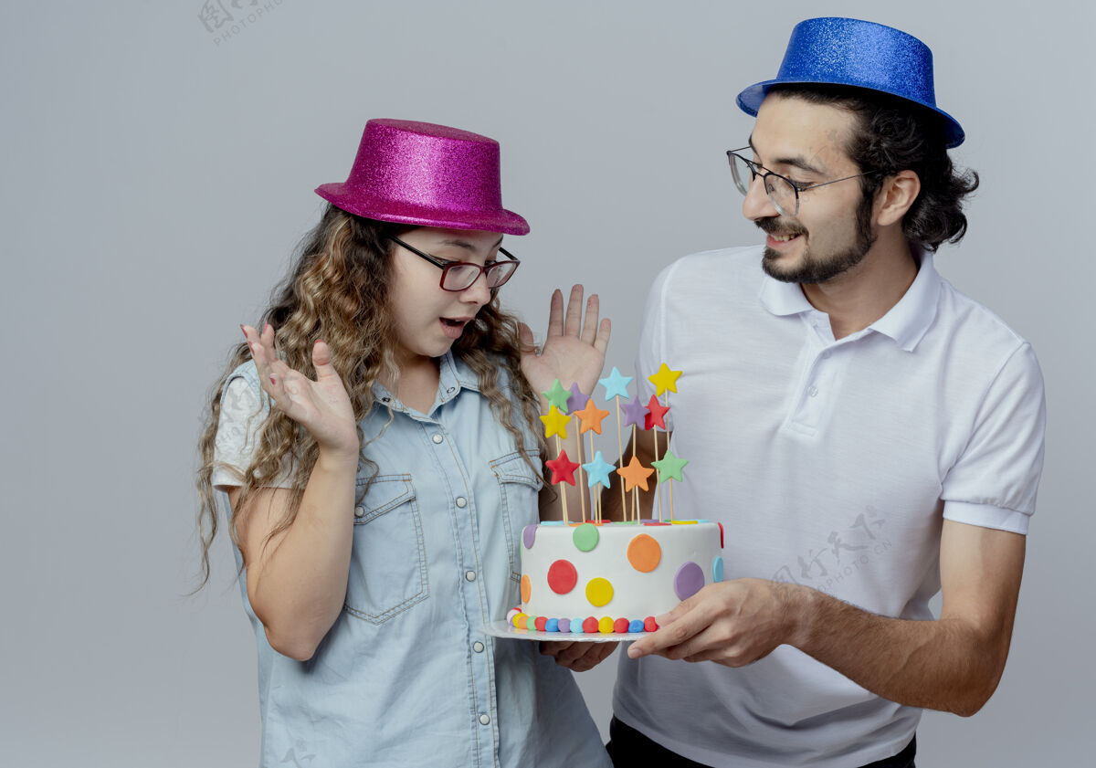 惊喜小两口戴着粉蓝相间的帽子高兴的家伙把生日蛋糕送给了惊讶的女孩孤立在白色的女孩男孩年轻人
