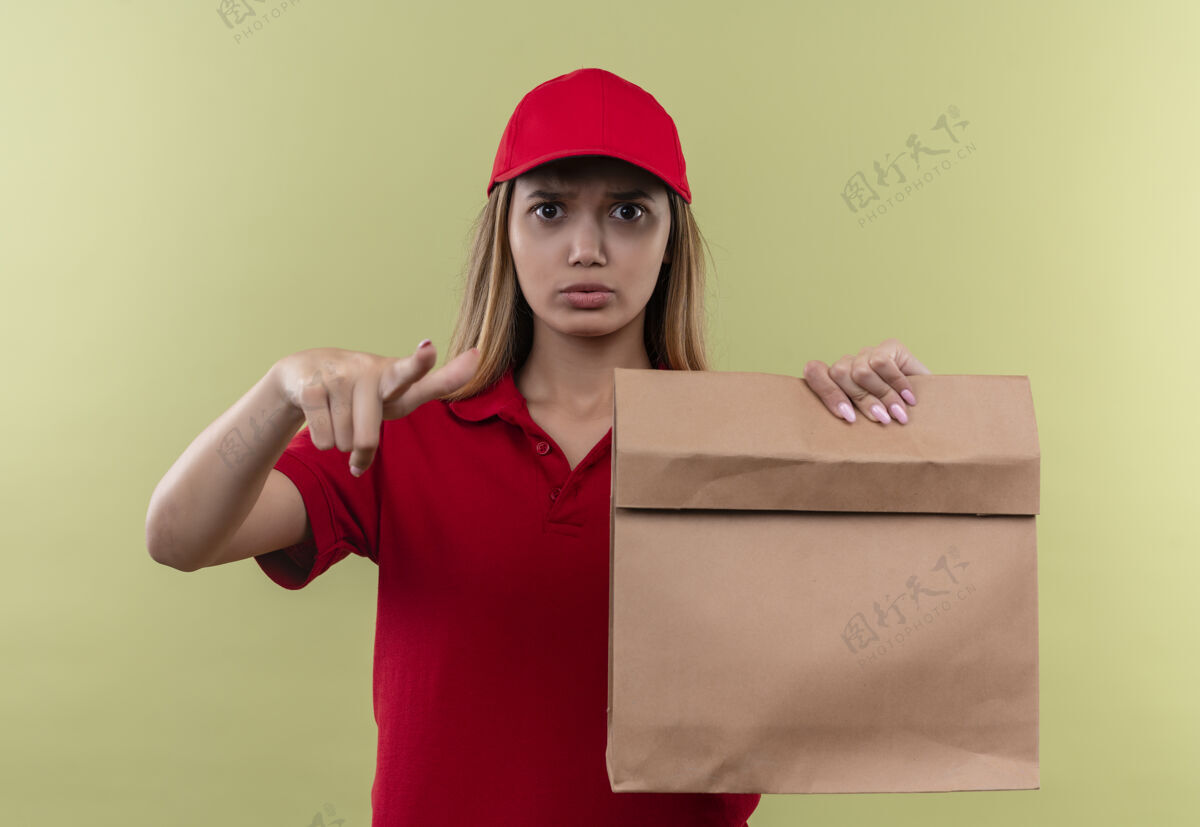 年轻严格的年轻送货女孩穿着红色制服 戴着帽子拿着纸袋 向你展示绿色的姿态女人包严格