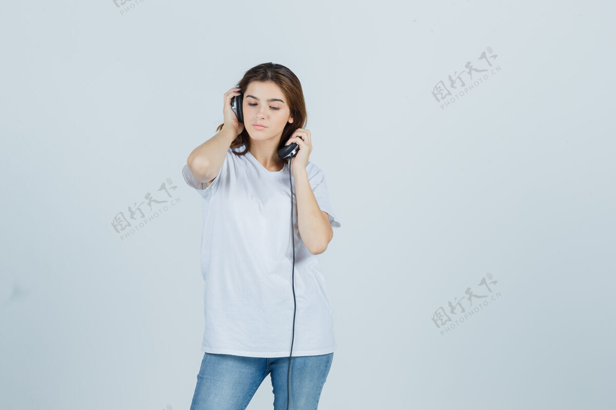 前面身穿白色t恤 牛仔裤的年轻女性摘下耳机 神情沉思 俯瞰前方护理牛仔裤人